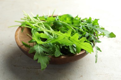 Photo of Many fresh arugula leaves in bowl on grey textured table, closeup