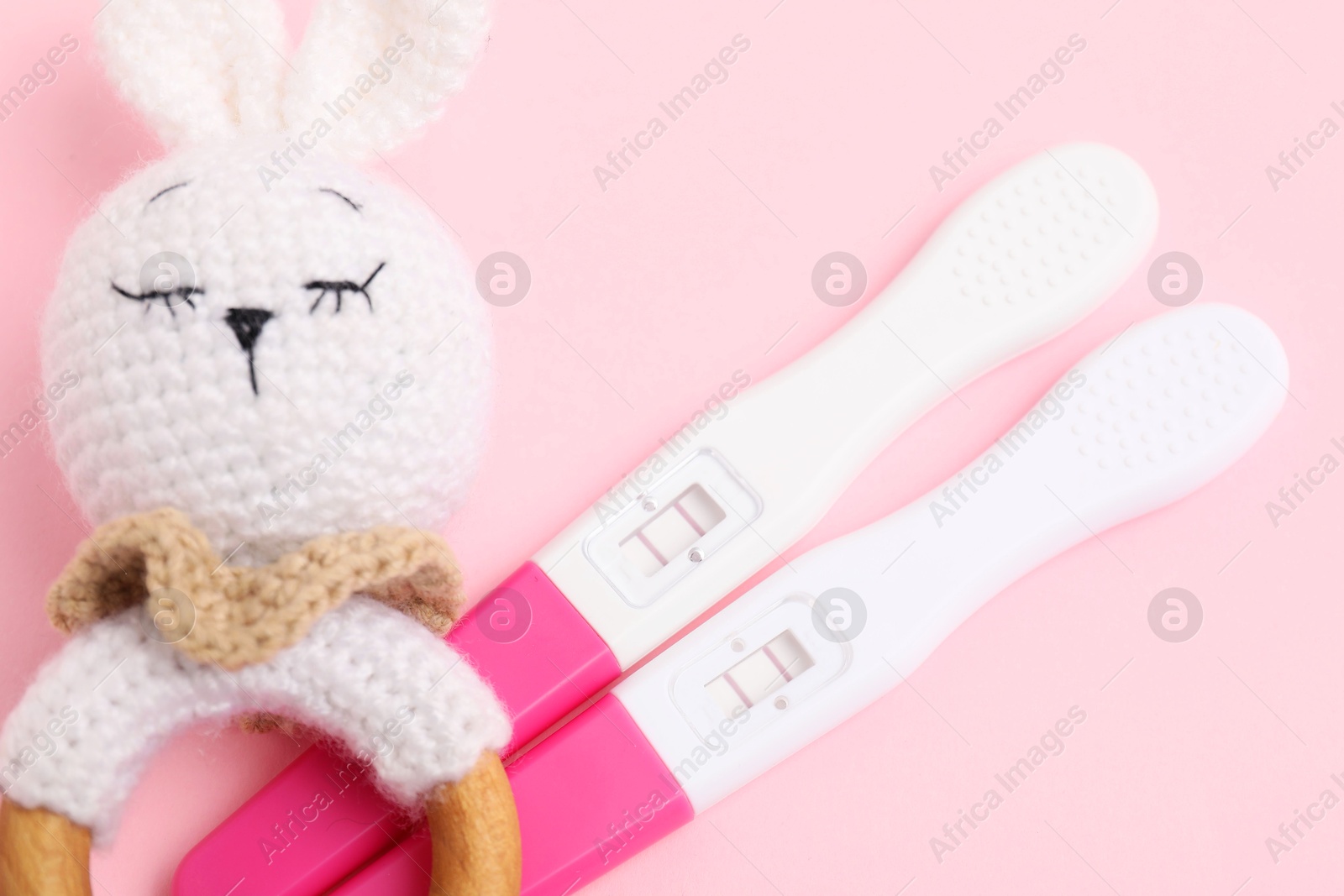 Photo of Pregnancy tests and baby rattle on pink background, closeup