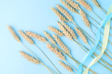 Photo of Ears of wheat with ribbons in colors of Ukrainian national flag on light blue background, flat lay