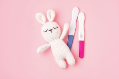 Photo of Pregnancy tests and toy bunny on pink background, top view