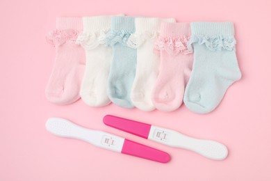 Photo of Pregnancy tests and socks on pink background, flat lay