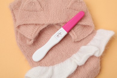 Photo of Pregnancy test and baby clothes on pale orange background, above view