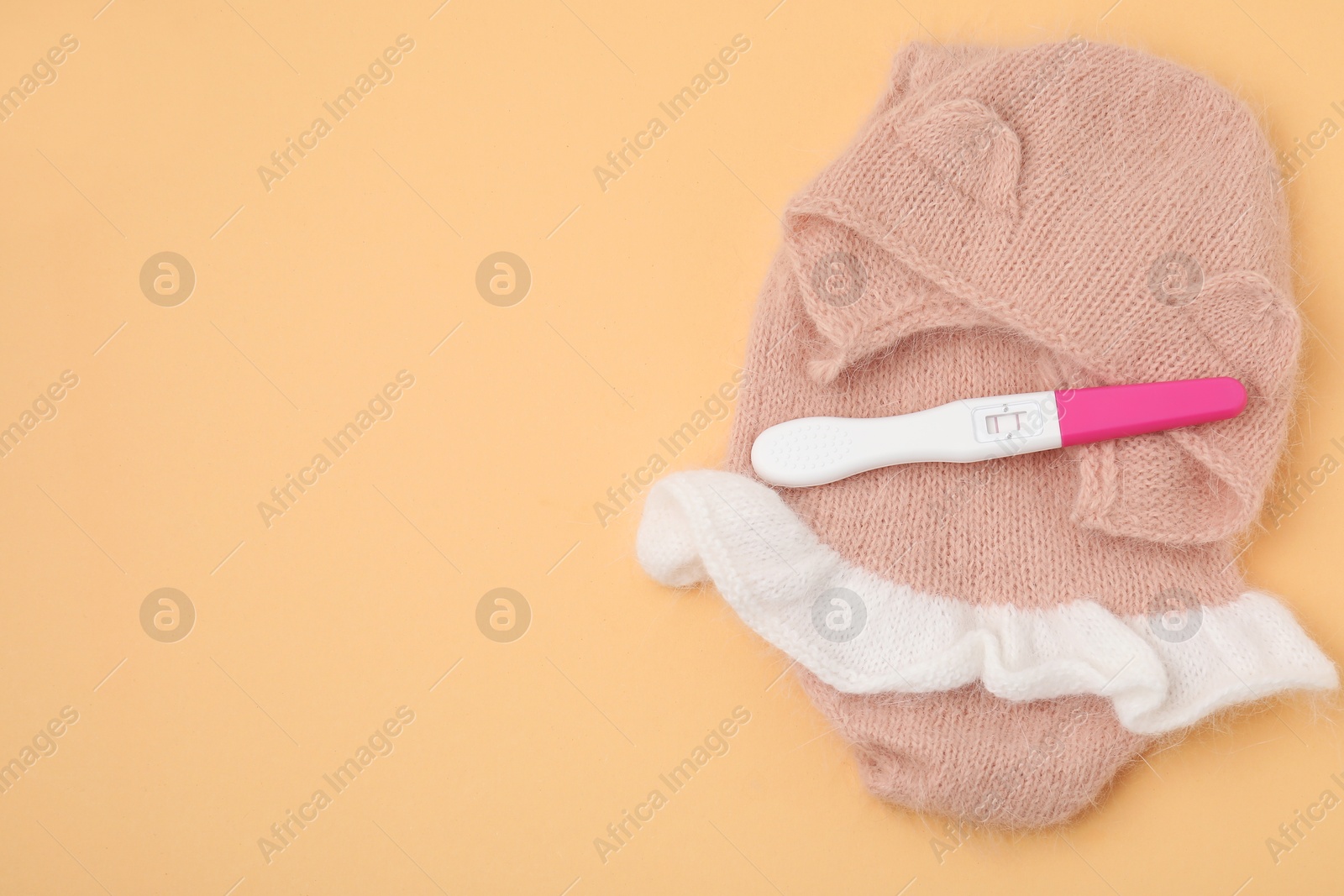 Photo of Pregnancy test and baby clothes on pale orange background, top view. Space for text