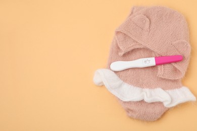 Photo of Pregnancy test and baby clothes on pale orange background, top view. Space for text