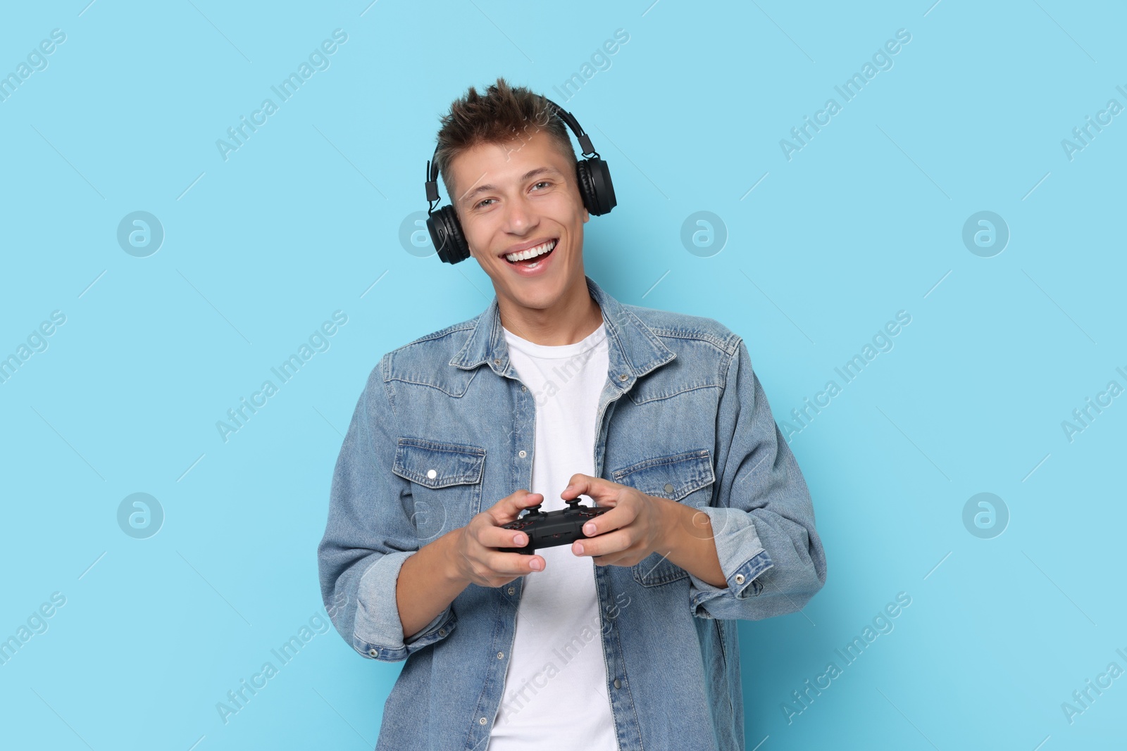 Photo of Happy young man playing video games with controller on light blue background