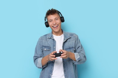 Happy young man playing video games with controller on light blue background