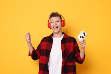 Happy young man in headphones with controller on orange background