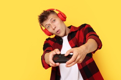 Young man in headphones playing video games with controller on orange background