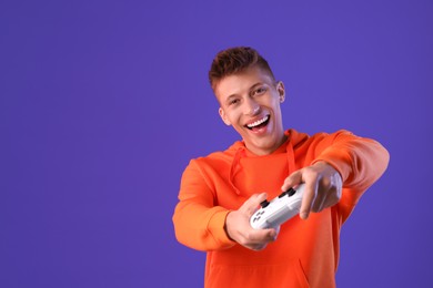 Photo of Happy young man playing video games with controller on violet background, space for text