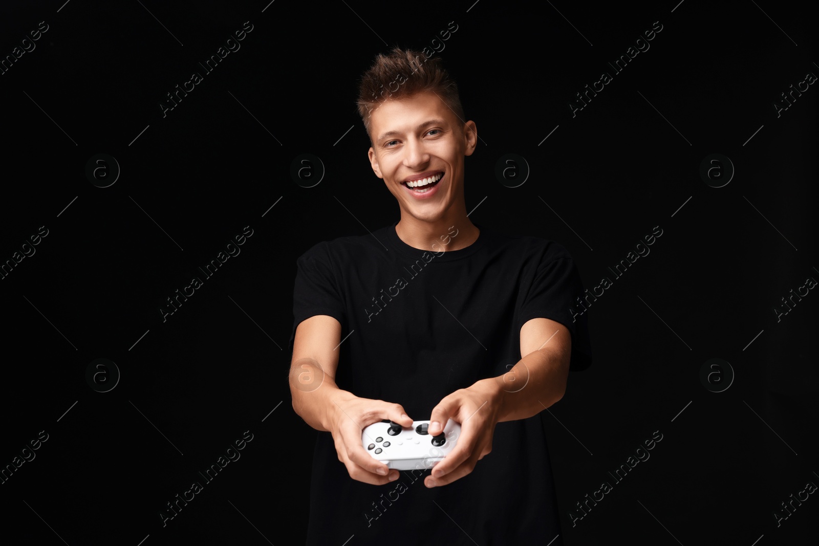 Photo of Happy young man playing video games with controller on black background