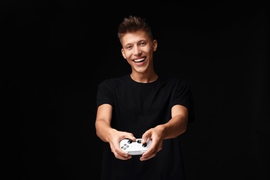 Photo of Happy young man playing video games with controller on black background