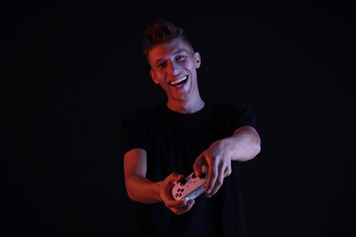 Photo of Happy young man playing video games with controller on black background