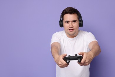 Young man in headphones playing video games with controller on violet background