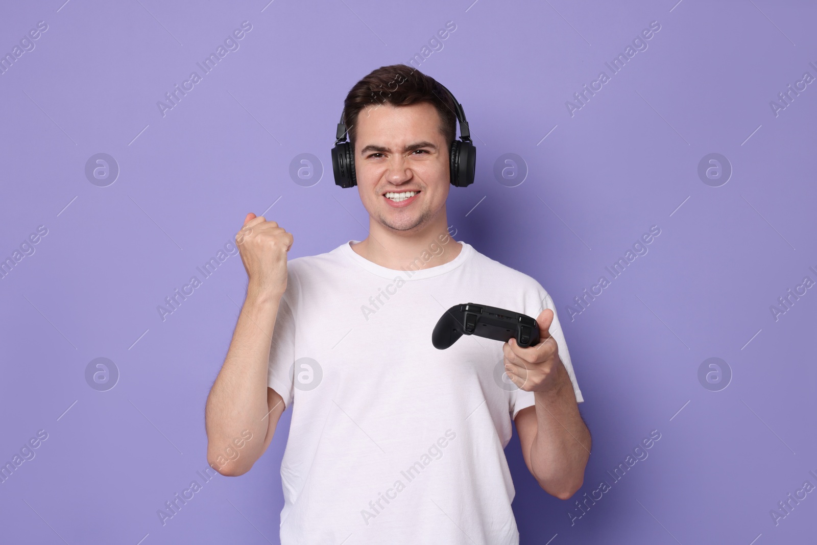 Photo of Happy young man in headphones with controller on violet background