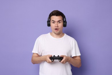 Young man in headphones playing video games with controller on violet background