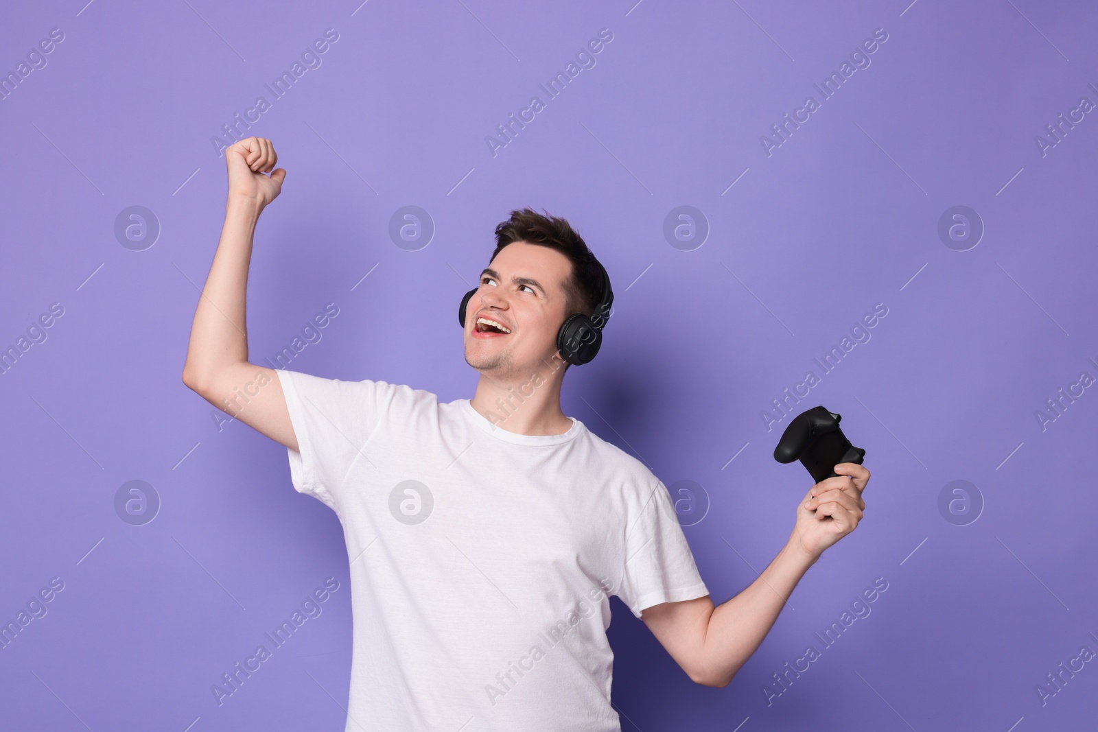 Photo of Happy young man in headphones with controller on violet background