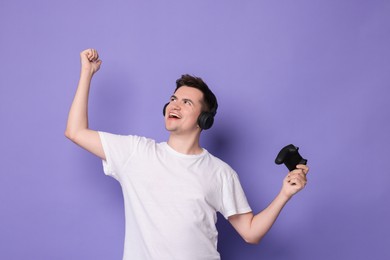 Photo of Happy young man in headphones with controller on violet background