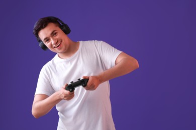 Happy young man in headphones playing video games with controller on violet background