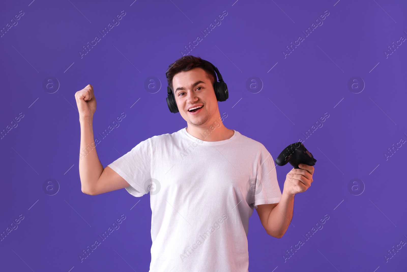 Photo of Happy young man in headphones with controller on violet background