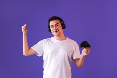 Photo of Happy young man in headphones with controller on violet background