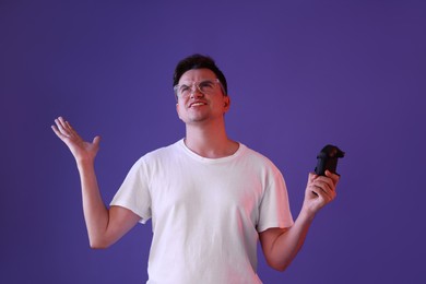 Unhappy young man with controller on violet background