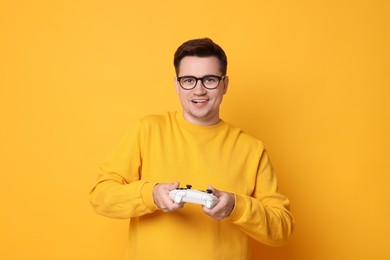 Happy young man playing video games with controller on orange background