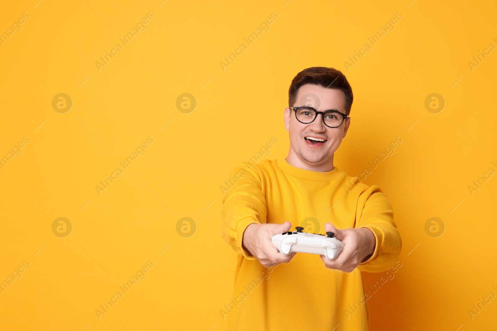 Photo of Happy young man playing video games with controller on orange background, space for text