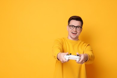 Happy young man playing video games with controller on orange background, space for text