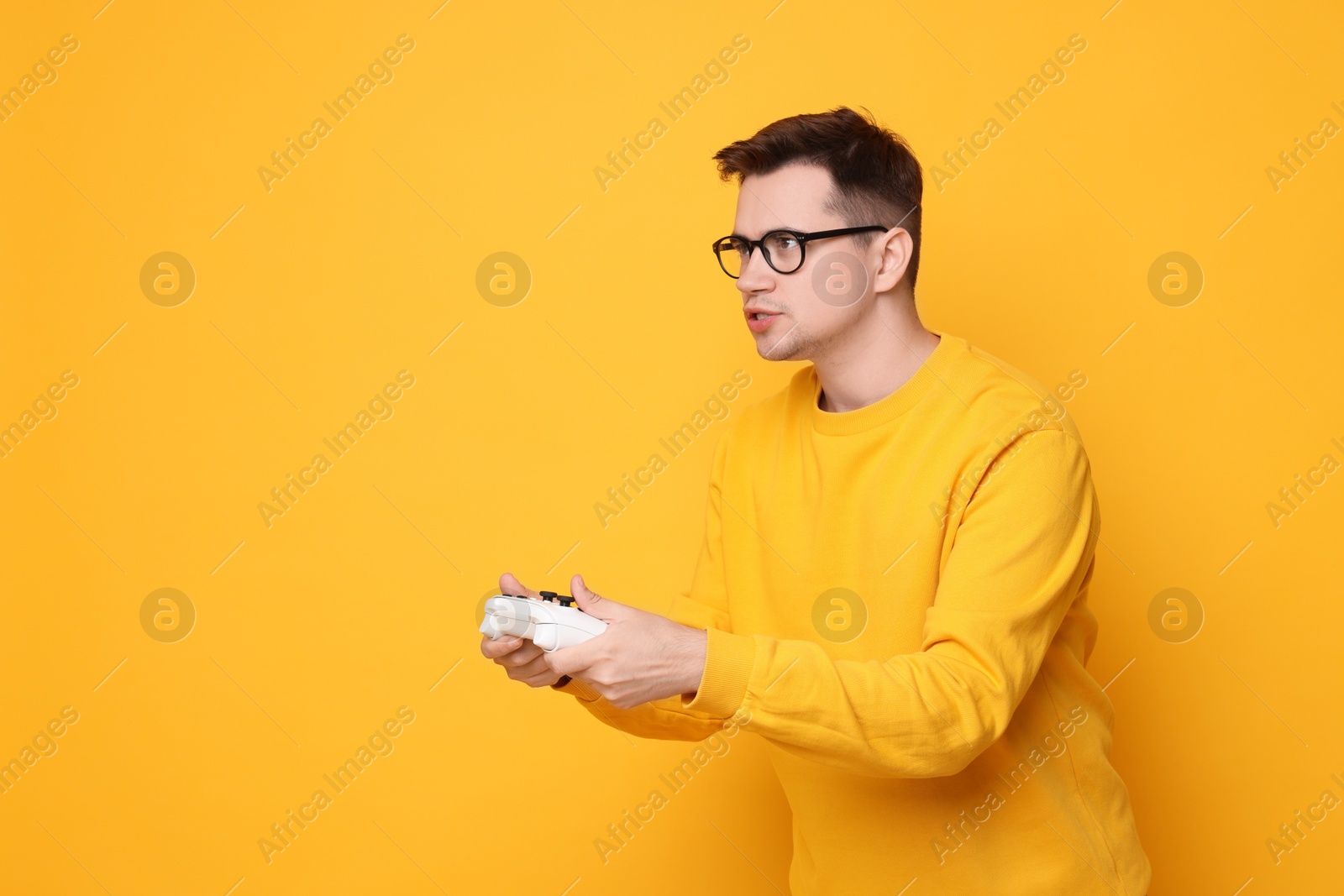 Photo of Young man playing video games with controller on orange background, space for text