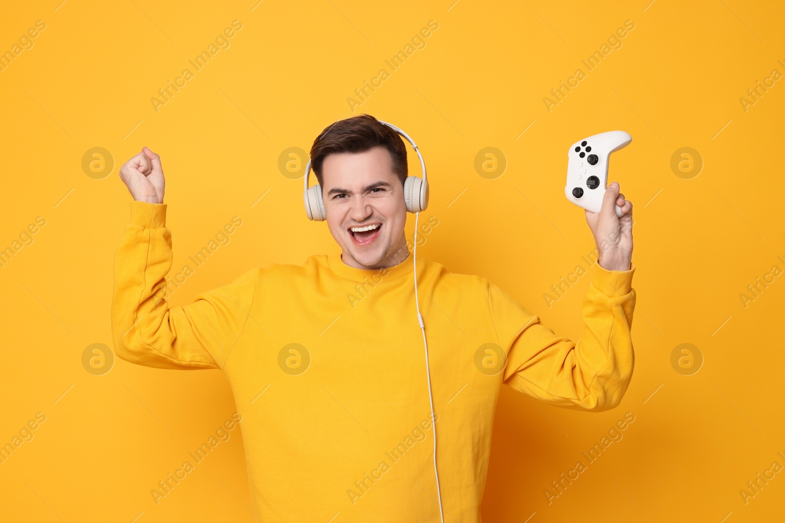 Photo of Young man in headphones with controller on orange background