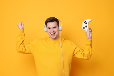 Young man in headphones with controller on orange background