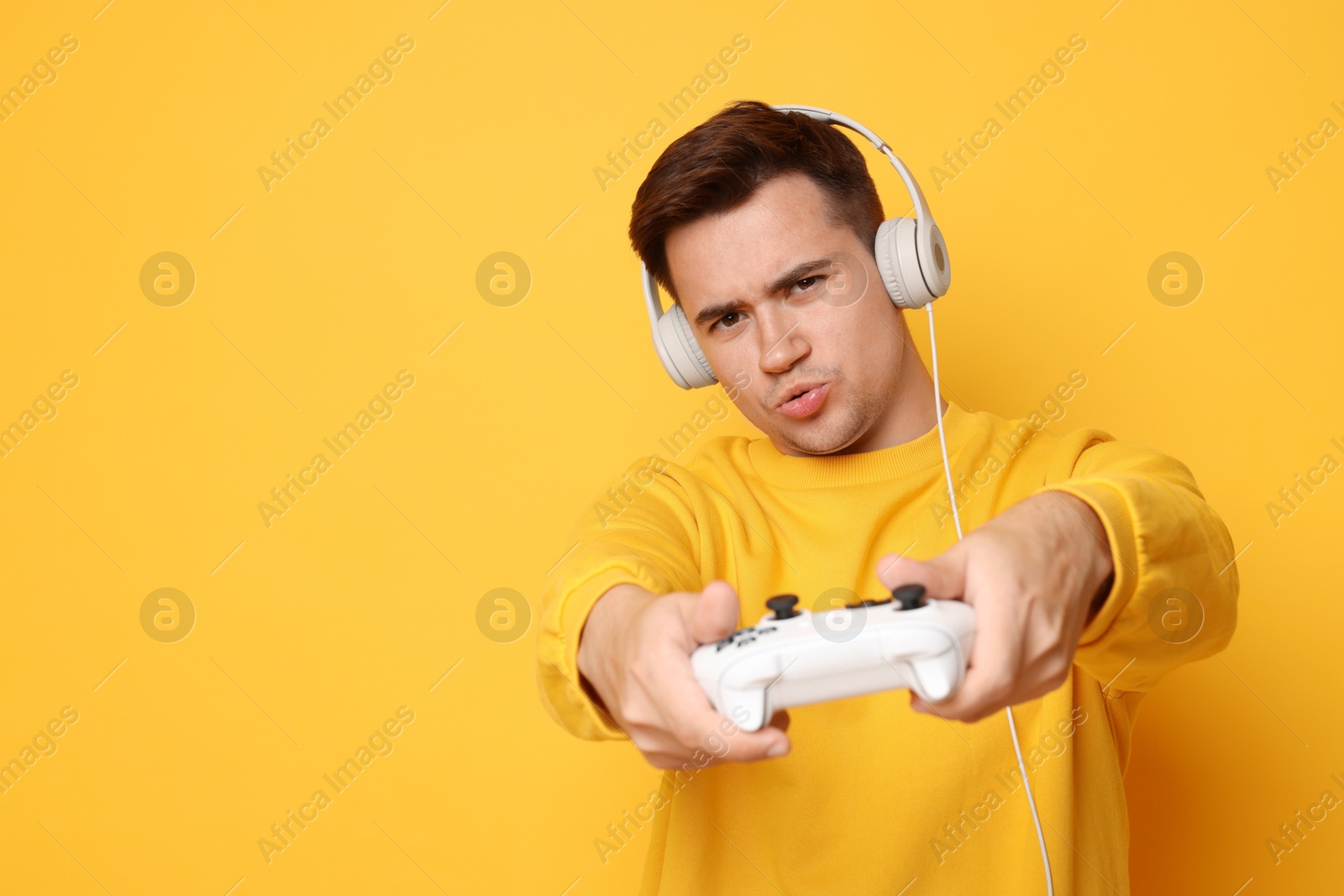 Photo of Young man in headphones playing video games with controller on orange background, space for text