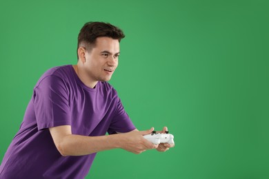 Happy young man playing video games with controller on green background, space for text