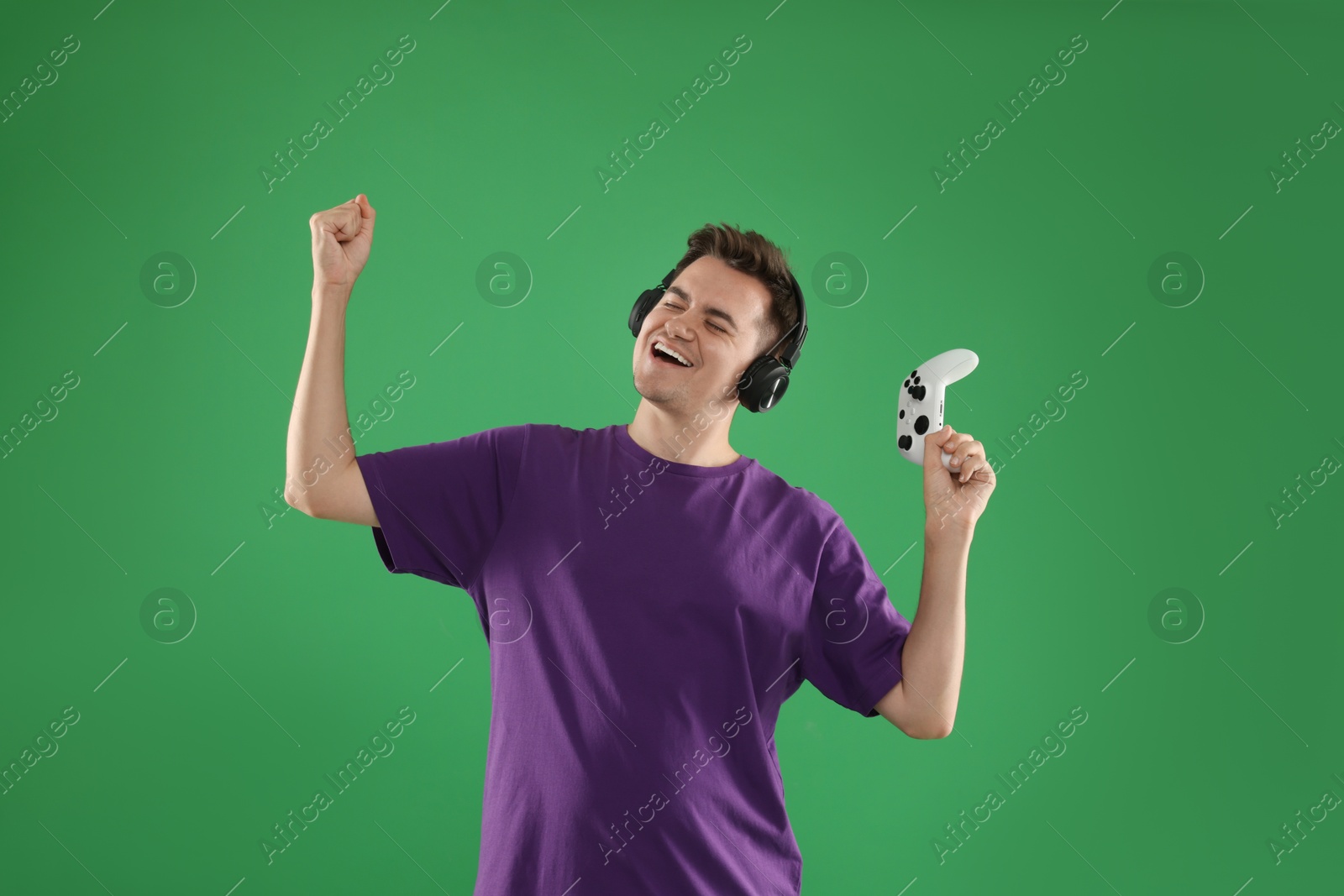 Photo of Happy young man in headphones with controller on green background