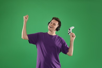 Happy young man in headphones with controller on green background