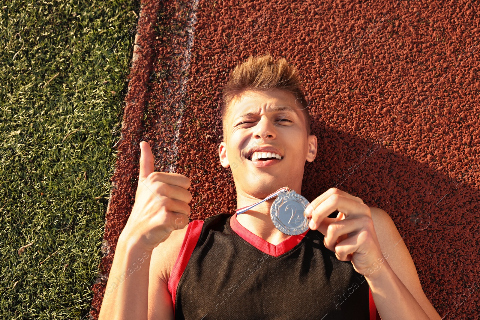 Photo of Happy winner with silver medal showing thumbs up at stadium