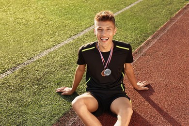 Happy winner with different medals sitting at stadium on sunny day