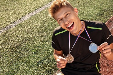 Happy winner with different medals sitting at stadium on sunny day. Space for text