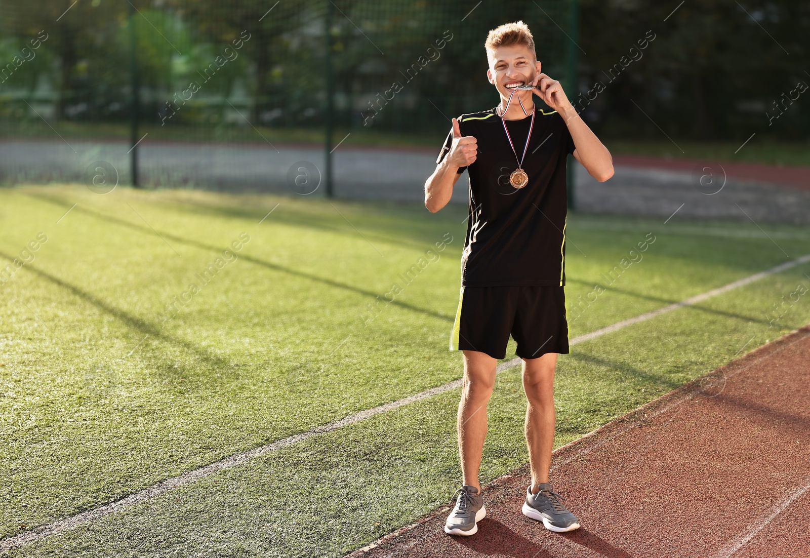 Photo of Happy winner with different medals showing thumbs up at stadium on sunny day. Space for text