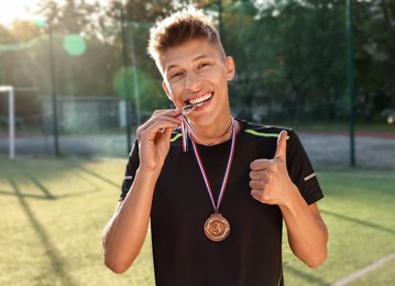 Photo of Happy winner with different medals showing thumbs up at stadium on sunny day