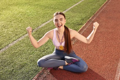 Photo of Happy winner with golden medal sitting at stadium on sunny day