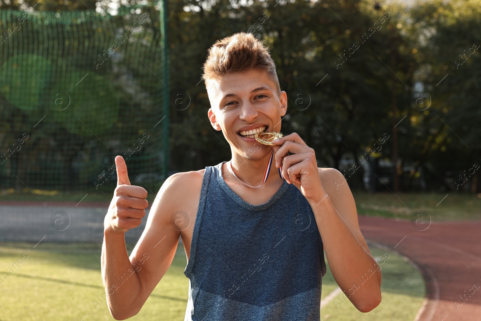 Photo of Happy winner with golden medal showing thumbs up at stadium