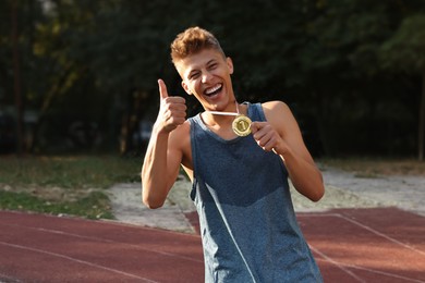 Happy winner with golden medal showing thumbs up at stadium