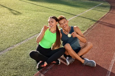 Happy winners with medals sitting at stadium on sunny day