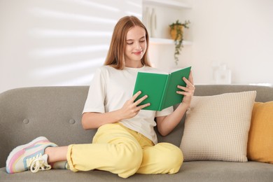 Teenage girl reading book on sofa at home