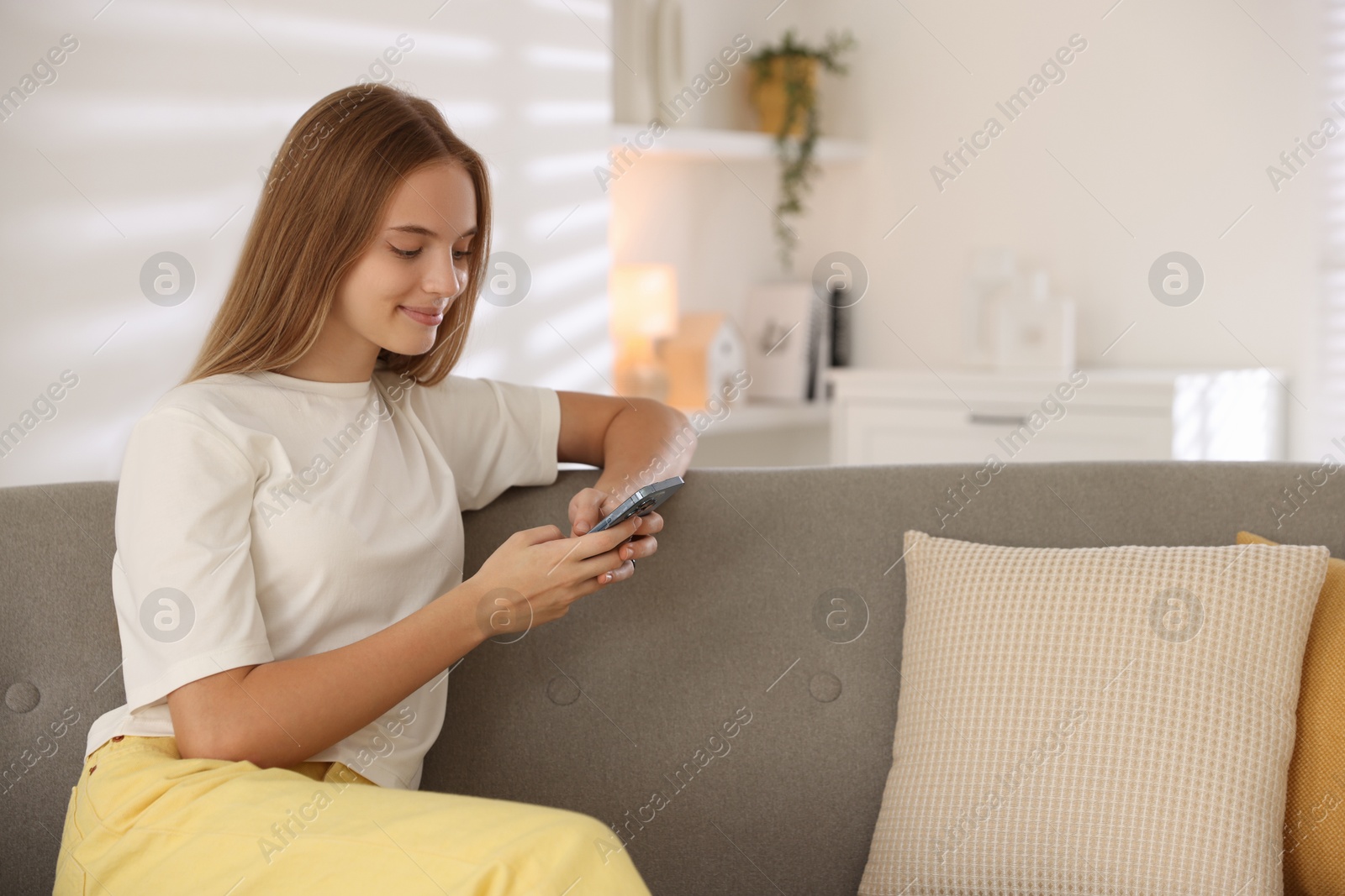 Photo of Teenage girl using smartphone on sofa at home