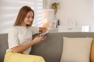 Teenage girl using smartphone on sofa at home