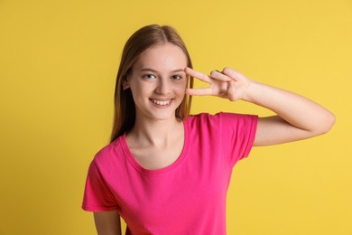 Teenage girl showing v-sign on yellow background