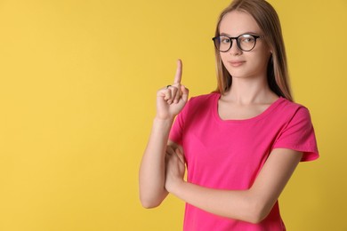 Portrait of teenage girl in glasses on yellow background, space for text