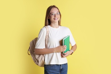 Photo of Teenage girl with books and backpack on yellow background